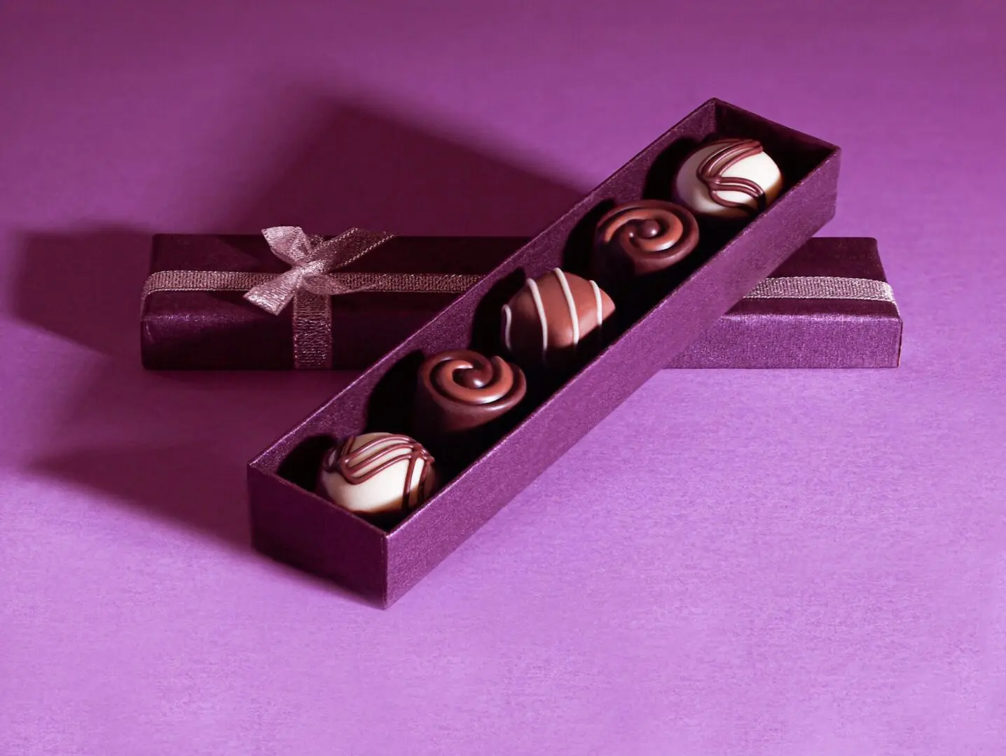 Four chocolates in a purple box on a purple background.